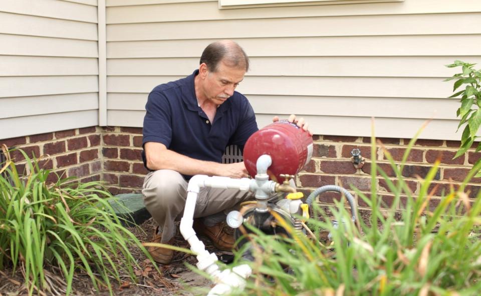 A man checking the well pump outside of a residential house.