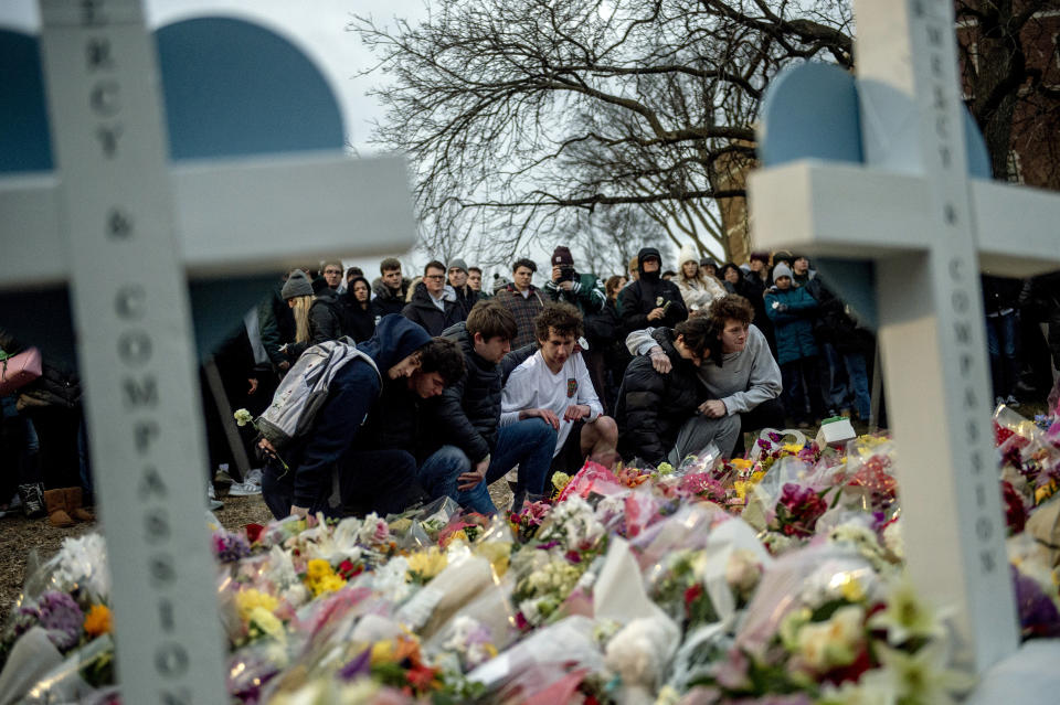 Michigan State University students kneel at an ever-growing bed of flowers and keepsakes dedicated to the students killed and injured in Monday's shootings on campus, as a crowd gathers at The Rock, a popular college landmark on Wednesday, Feb. 15, 2023, at Michigan State University in East Lansing, Mich. (Jake May/The Flint Journal via AP)