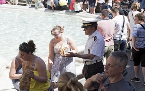 A police officer tells tourists not to eat or sit on the rim of the fountain - Credit: EPA