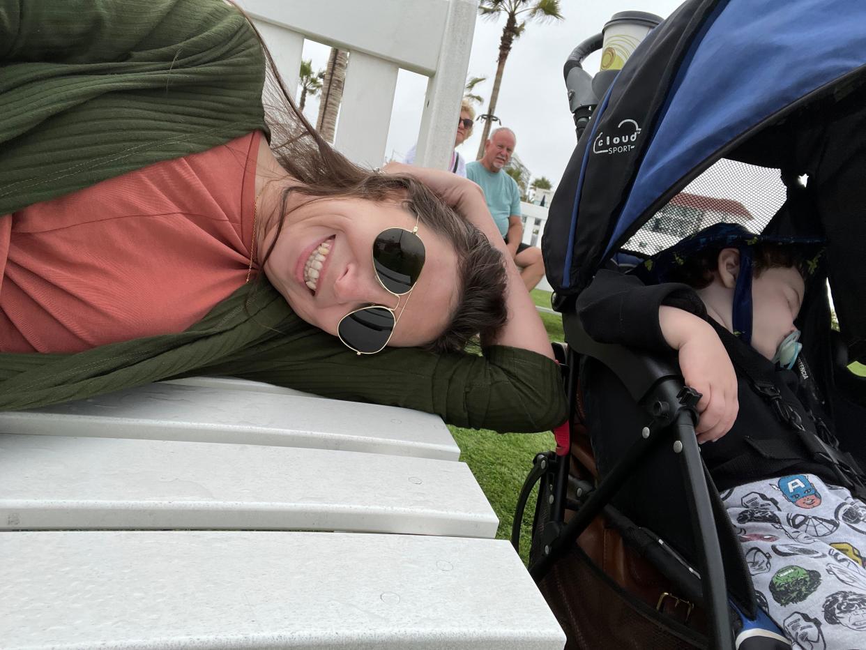 Samantha Brandon, lying down on a bench outside wearing sunglasses next to her child in a stroller