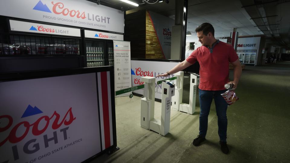 At a concession stand inside Ohio Stadium, Mike Muffler demonstrates Amazon's Just Walk Out technology designed to eliminate checkout lines. Guests at the Buckeye Country Superfest buy concessions by entering their credit card and hovering their palm over an Amazon One device inside the stadium. The technology detects what shoppers take from or return to the shelves and creates a virtual shopping session. Guests can grab what they need and leave the store without having to wait in line to checkout.