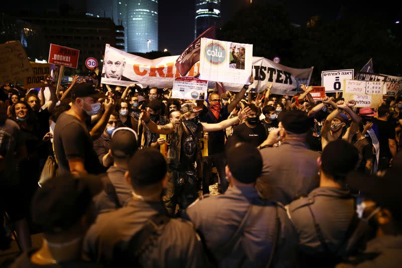 Police force stand in front of the protestors as they block a main junction in the city following a protest against the government's response to the financial fallout of the coronavirus disease (COVID- 19) crisis in Tel Aviv