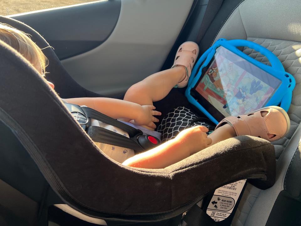 A child sitting in a car seat watching a blue iPad.