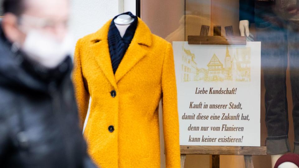 Eine Person mit Mund-Nasen-Schutz geht am Schaufenster eines Bekleidungsgeschäfts vorbei.