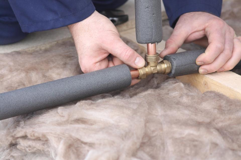 Person wearing a blue coat putting foam insulation on copper pipes.