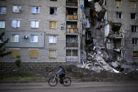 A woman rides a bicycle past a residential building heavily damaged in a Russian bombing in Bakhmut, eastern Ukraine, Tuesday, May 24, 2022. The town of Bakhmut has been coming under increasing artillery strikes, particularly over the last week, as Russian forces try to press forward to encircle the city of Sieverodonetsk to the northeast. (AP Photo/Francisco Seco)