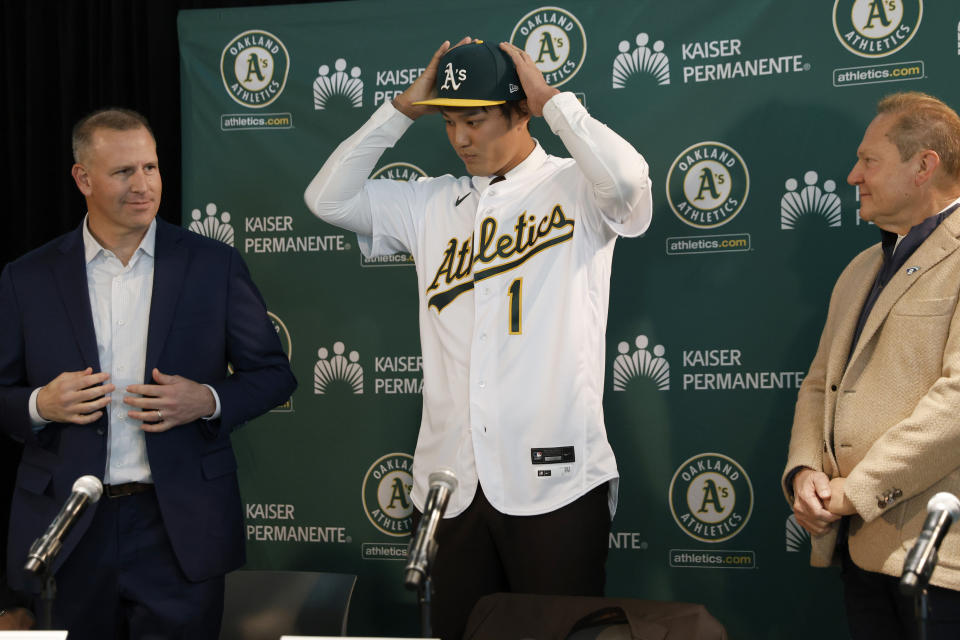 Oakland Athletics pitcher Shintaro Fujinami, center, puts on a jersey and hat with Athletics' general manager David Forst, left, and agent Scott Boras, right, during his introductory baseball news conference in Oakland, Calif., Tuesday, Jan. 17, 2023. (AP Photo/Jed Jacobsohn)