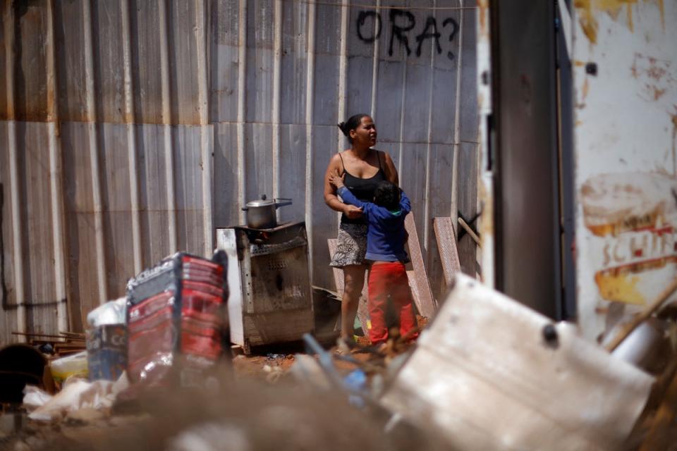 Luciana stands with her son, as she cooks using firewood outside her home (Reuters)