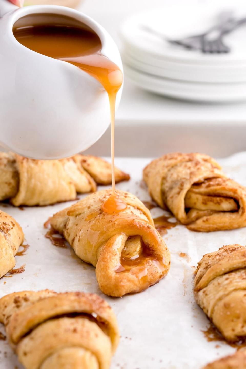 Pouring caramel sauce onto apple pie crescent roll bites.