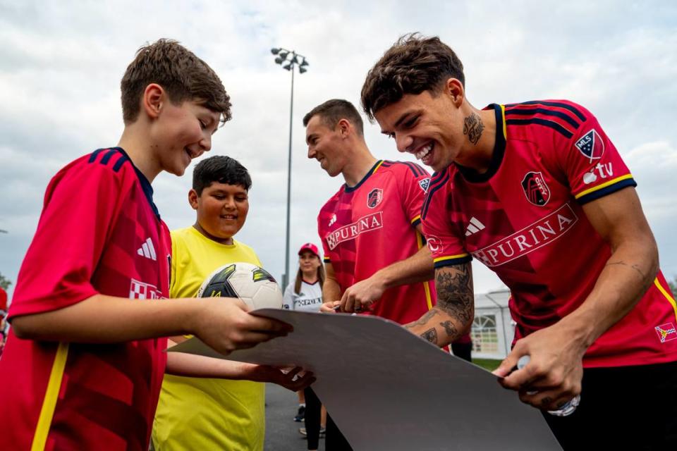 St. Louis City SC midfielder Célio Pompeu (12) signs an autograph on a poster held by Noah White, 12, of Collinsville, on Thursday, Oct. 26, 2023, during the dedication of a St. Louis City SC mini pitch at Granby Park in Fairmont City. Israel Aguirre, 10, of Collinsville, watches while standing next to St. Louis City SC defender Kyle Hiebert (22). Brian Munoz/Brian Munoz