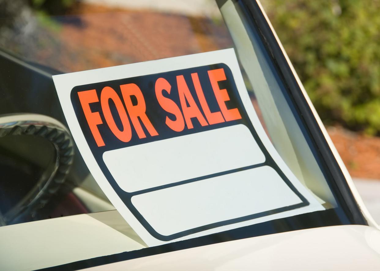 Closeup view of blank red and white paper for sale sign in window of white car.