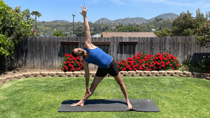 Man on a yoga mat outside practicing yoga for tall people in Triangle Pose