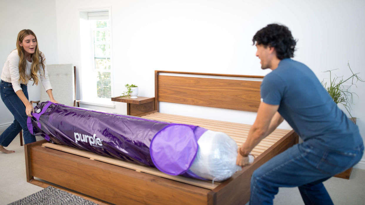  A man and a woman remove a Purple mattress from its packaging before it starts to expand, ready for sleeping on later. 