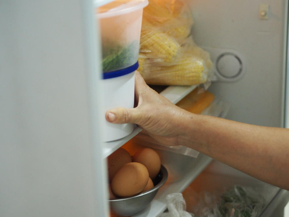 Person's hand opening a refrigerator stocked with eggs and vegetables, implying budget-friendly meal planning