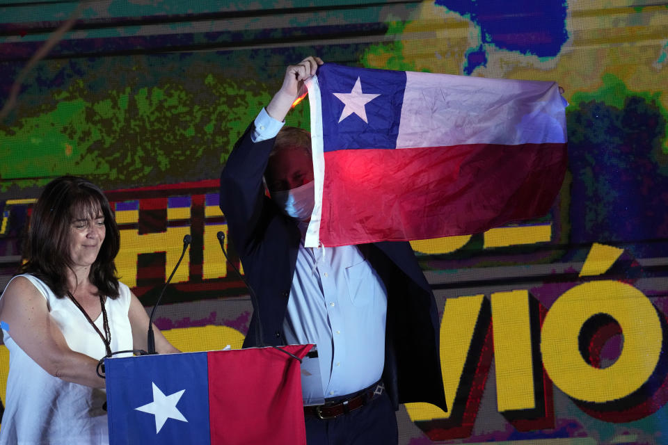 Republican Party presidential candidate Jose Antonio Kast and his wife Maria Pia Adriasola hold up Chilean flags toward supporters at his campaign headquarters after polls closed and partial results were announced in Santiago, Chile, Sunday, Nov. 21, 2021. (AP Photo/Esteban Felix)