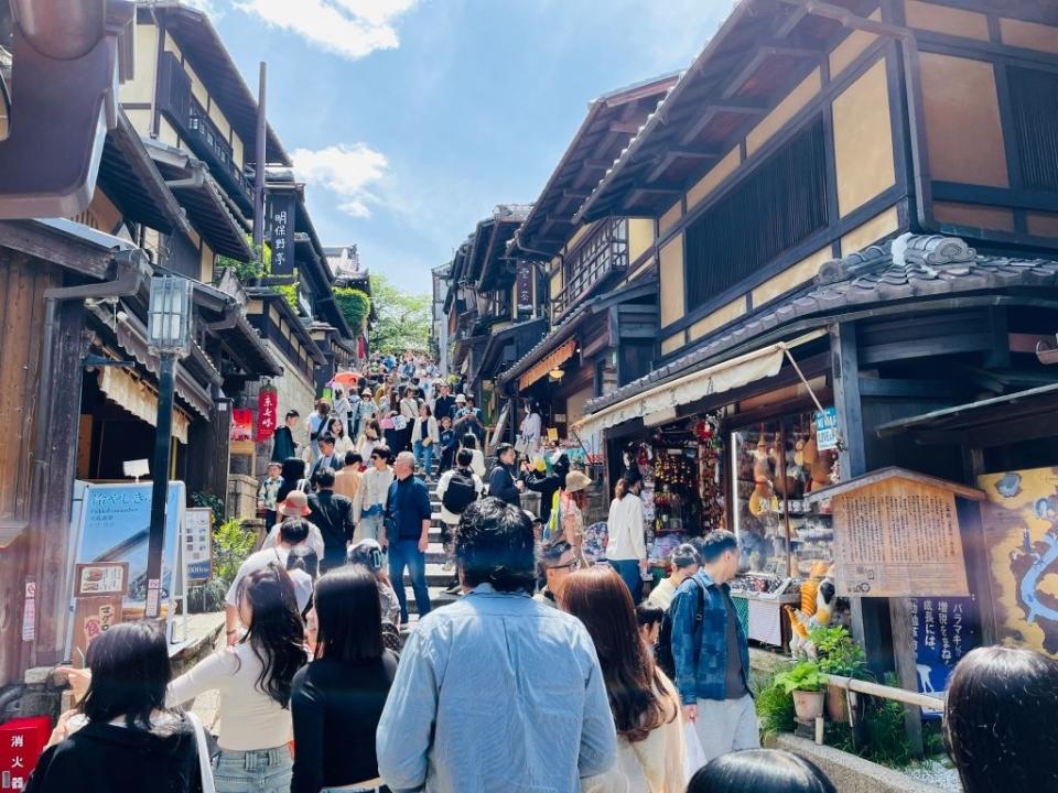 People walk down a bustling traditional Japanese street lined with wooden buildings and shops under a bright sky. The image is used in a travel article