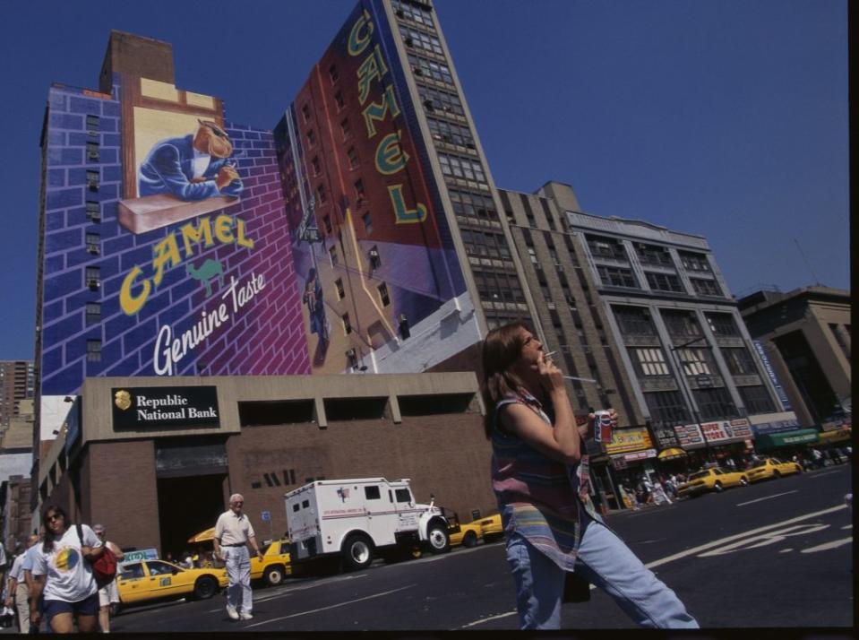 A female pedestrian smoking a cigarette walks past a large mural for Camel cigarettes on the side of a building. (Photo by James Leynse/Corbis via Getty Images)