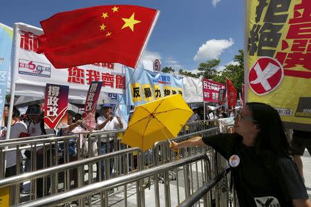 A pro-democracy protester carrying a yellow umbrella, symbol of the Occupy Central movement, demonstrates in front of pro-China supporters waving a Chinese national flag outside Legislative Council in Hong Kong, China June 17, 2015. REUTERS/Bobby Yip