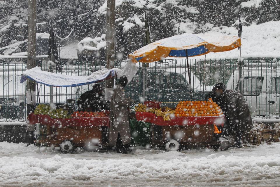 Kashmiri fruit venders await customers as it snows in Srinagar, India, Tuesday, March 11, 2014. The Kashmir valley was Tuesday cut off from rest of India due to heavy snowfall. (AP Photo/Mukhtar Khan)
