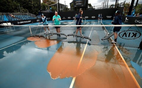 Staff are seen attempting to clean dirt off the outside courts, caused by rainfall in the Melbourne area  - Credit: GETTY IMAGES