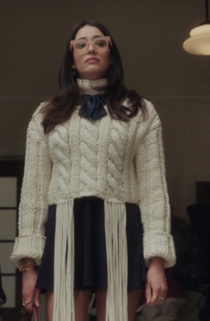 Luna wears a dark high waisted ruffle skirt and a knit sweater with fringe on the hem