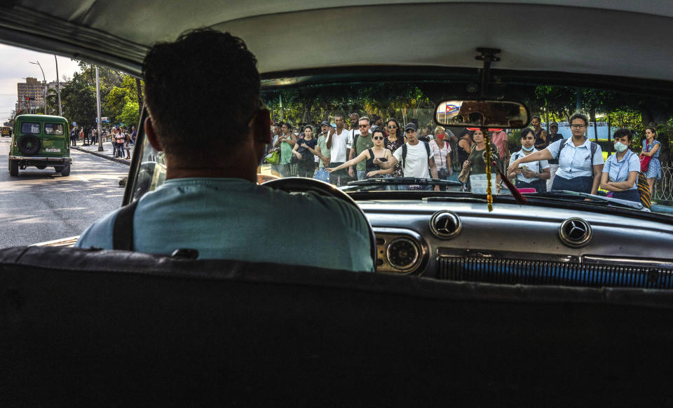 Las personas que esperan en una parada de transporte público le hacen señas a un taxi colectivo en La Habana, Cuba, el martes 4 de abril de 2023. (AP Foto/Ramón Espinosa)