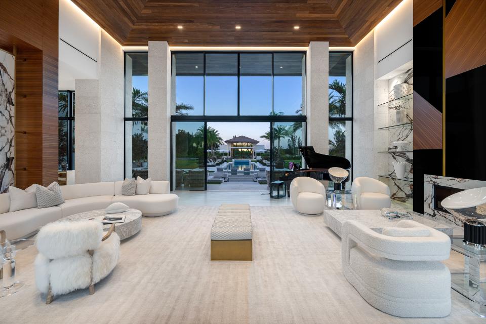 This fresh, white great room by Studio J & Co. welcomes guests with a hospitality feel and serves as a neutral backdrop to a deep blue lap pool and extravagant landscape. The 15,000-square-foot estate shares a mix of deep wood tones and coral stone with floor to ceiling windows and sliding doors bringing the outside in.