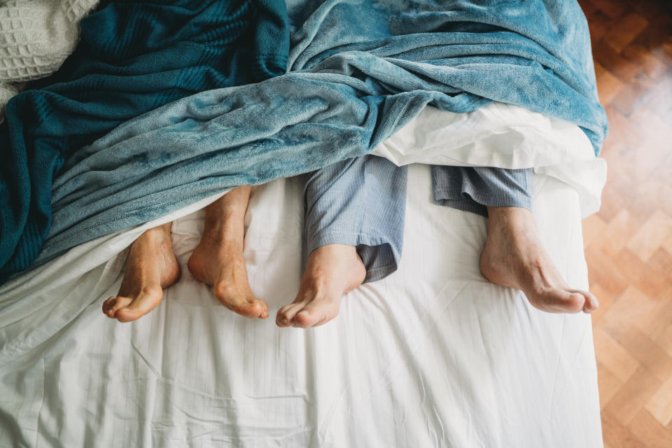 High angle view of feet lying down in bed. Senior couple lying down in bed, their feet come out from under the sheets.