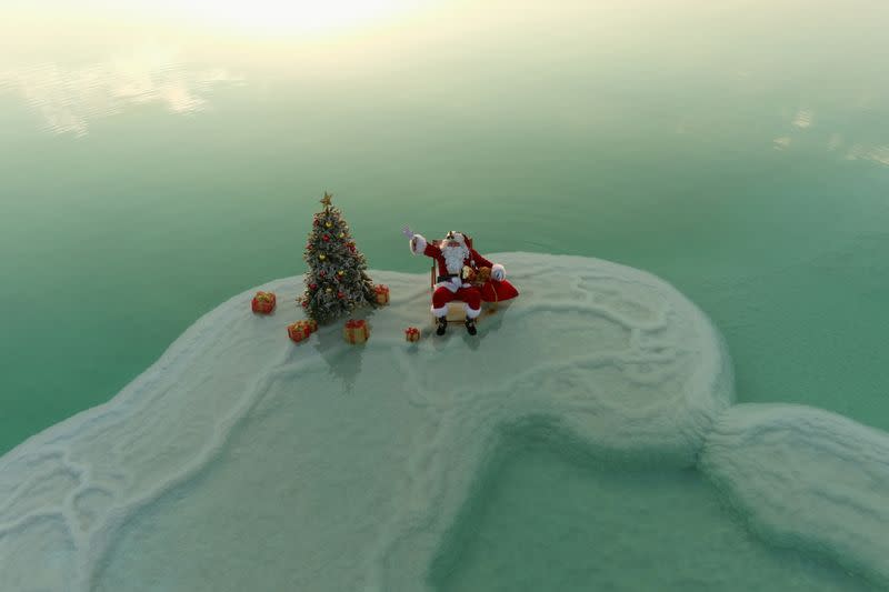 An aerial view shows Issa Kassissieh, wearing a Santa Claus costume, and sitting next to a Christmas tree while posing for a picture on a salt formation in the Dead Sea, near Ein Bokeq