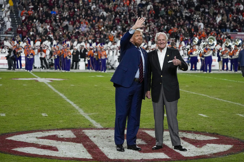 FILE - Republican presidential candidate and former President Donald Trump waves with South Carolina Gov. Henry McMaster during halftime in an NCAA college football game between the University of South Carolina and Clemson Saturday, Nov. 25, 2023, in Columbia, S.C. Trump has spent less time campaigning in early-voting states than many of his Republican primary rivals. But his campaign has been bolstering his schedule with appearances at major sporting events. Video of his appearances routinely rack up hundreds of thousands of views across social media. (AP Photo/Chris Carlson, File)