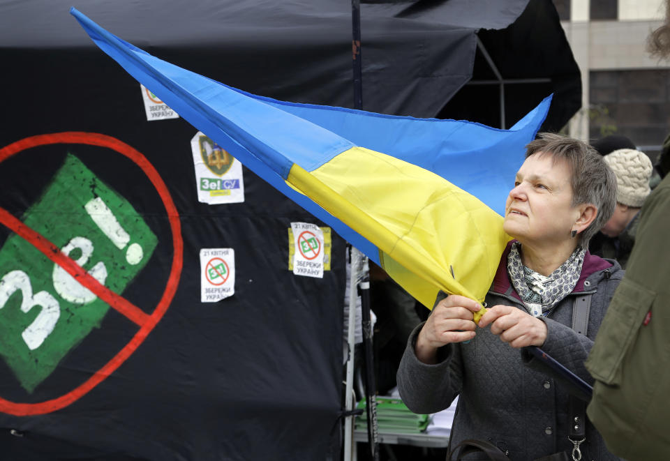 A woman holds an Ukrainian flag standing next to a tent of opponents of comedian and presidential candidate Volodymyr Zelenskiy in downtown Kiev, Ukraine, Wednesday, April 17, 2019. The second round of presidential vote in Ukraine will take place on April 21. (AP Photo/Sergei Grits)