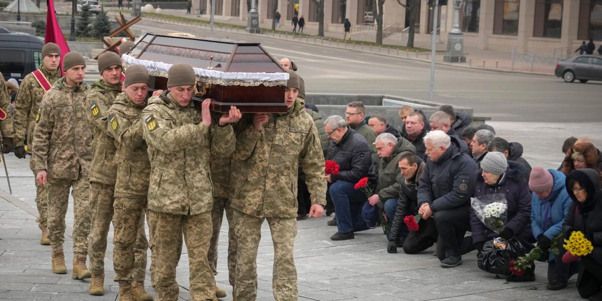 People kneel as the Ukrainian servicemen carry the coffin of their comrade Oleh Yurchenko killed in a battlefield with Russian forces in the Donetsk region during a commemoration ceremony in Independence Square in Kyiv, Ukraine, Sunday, Jan. 8, 2023.