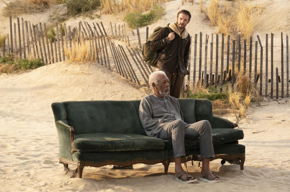 Morgan Freeman sitting on a couch in the sand and Dan Stevens behind him