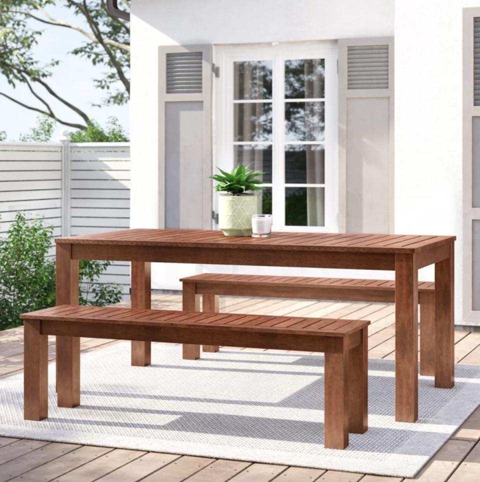 the medium wood table and benches on a beige rug in a decorated porch space