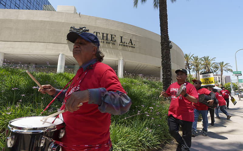 Striking hotel workers wearing red shirts and carrying drums and makeshift percussion instruments march outside the L.A. Grand Hotel Downtown