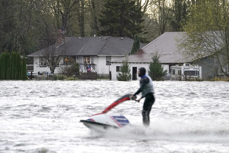 A man operates a personal watercraft in view of a home cut off by rising water from the Skagit River, Monday, Nov. 15, 2021, in Sedro-Woolley, Wash. (AP Photo/Elaine Thompson)