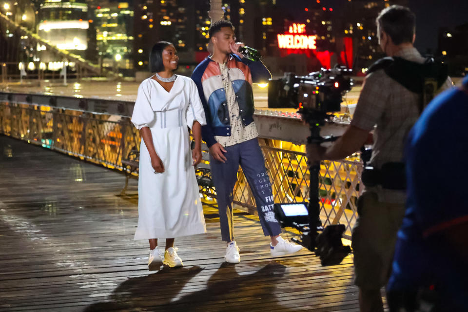 couple walking down a bridge drinking while cameras film in front of them