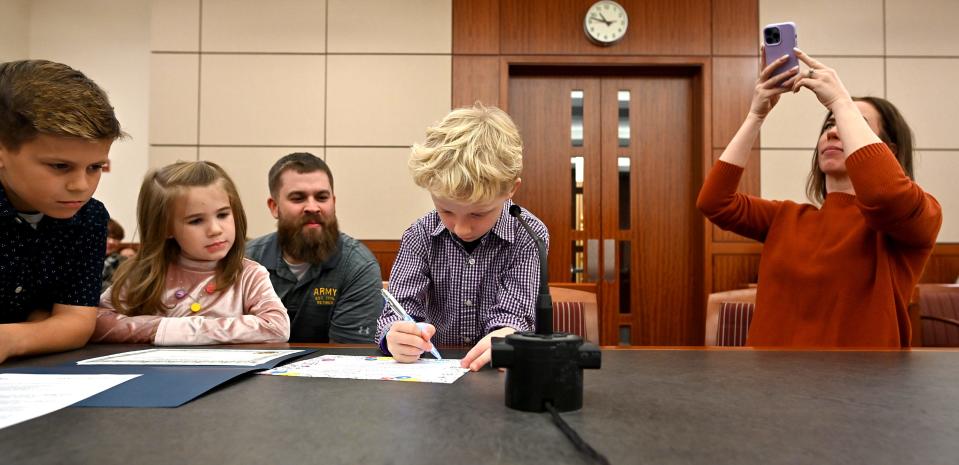 Haiden Orsi, 9, of Charlton signs his Certificate of Adoption with with his new family, mom, Hollie Asquith, and dad, Matthew McManaman, and siblings, Harper and Logan McManaman, during Friday's 20th annual National Adoption Day at Worcester Juvenile Court.