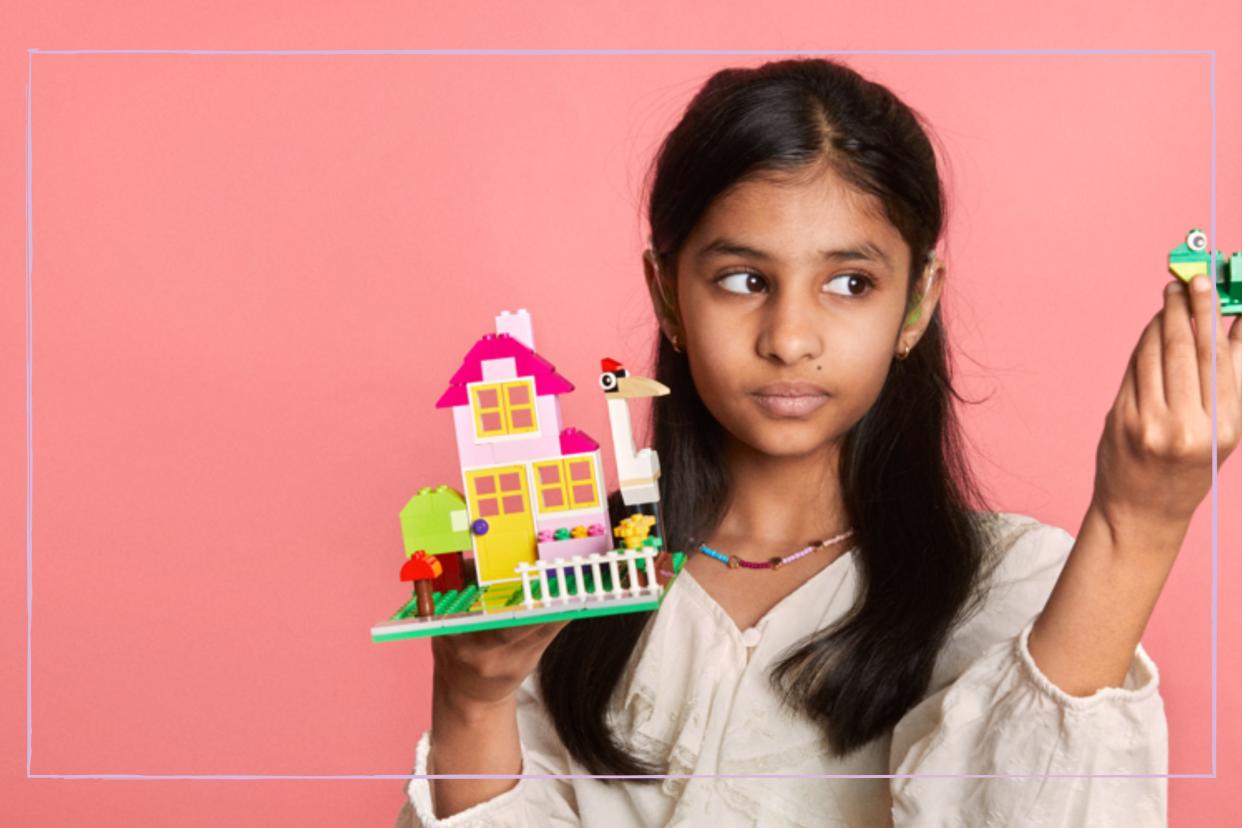  A girl holding up a LEGO creation against a pink background. 