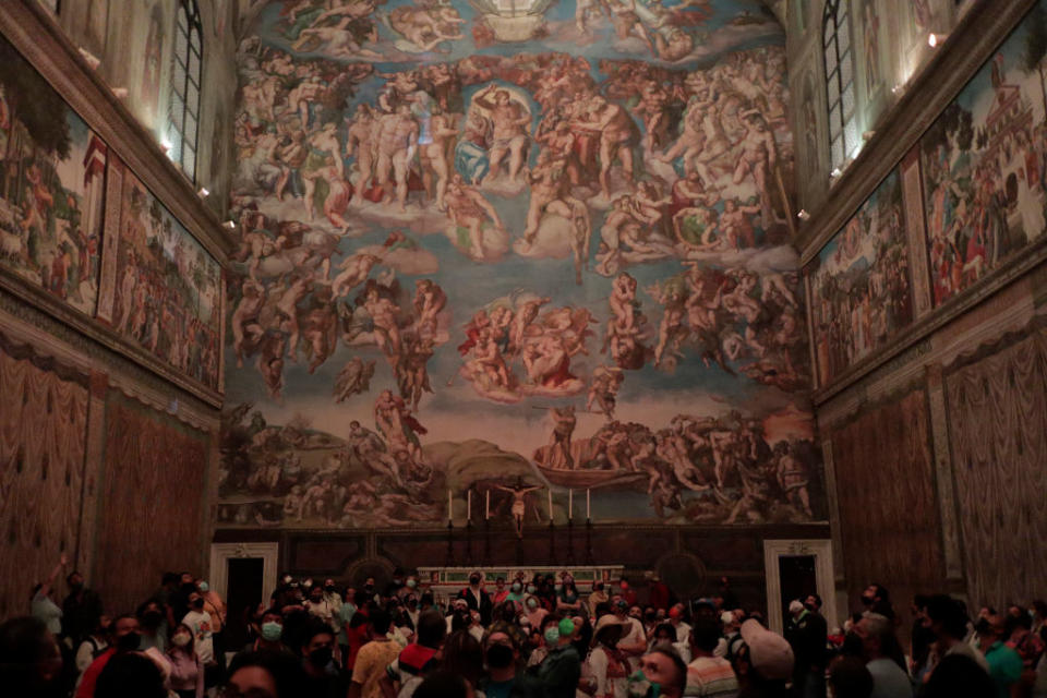 A large group of people touring the Sistine Chapel, featuring Michelangelo's famous frescoes on the ceiling and walls