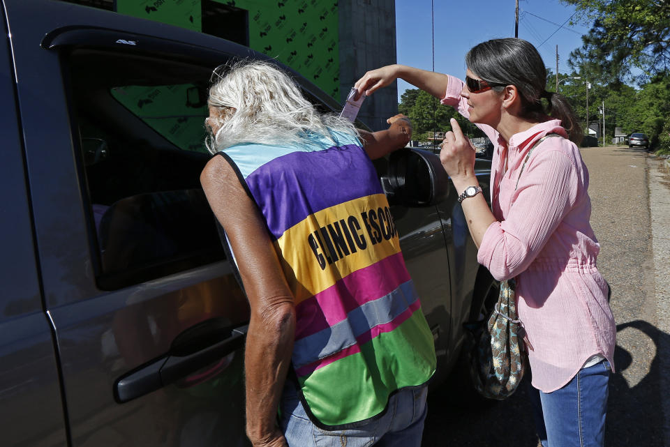 A clinic escort, left, speaks to a driver and patient while an abortion protester attempts to hand over some reading material outside the Jackson Women's Health Organization clinic in Jackson, Miss., Wednesday, April 10, 2019. The clinic is the only medical facility that performs abortions in the state. The state legislature recently passed a law that would ban most abortions after a fetal heartbeat is detected, meaning as early as six weeks. (AP Photo/Rogelio V. Solis)