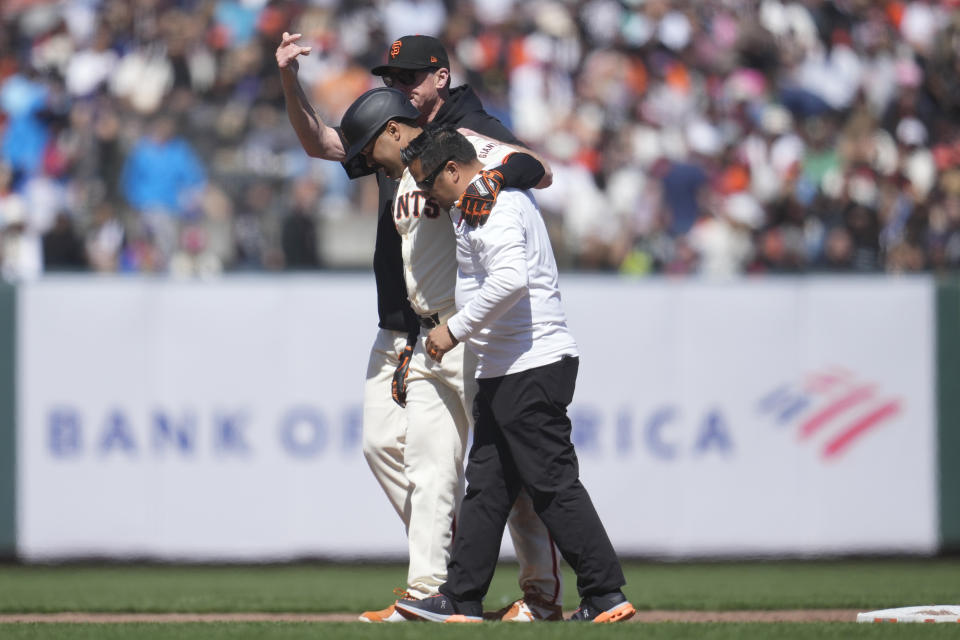 San Francisco Giants' LaMonte Wade Jr., middle, walks off the field with manager Bob Melvin, back, and a trainer after being injured on his double against the Philadelphia Phillies during the fifth inning of a baseball game in San Francisco, Monday, May 27, 2024. (AP Photo/Jeff Chiu)