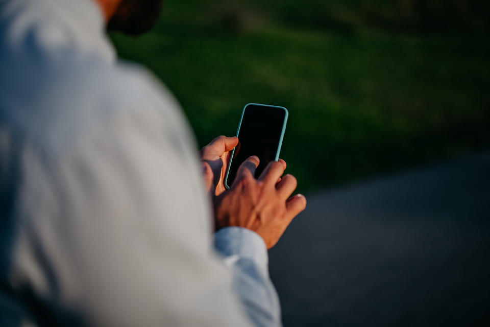 Back view of a man holding a blank iPhone and tapping it