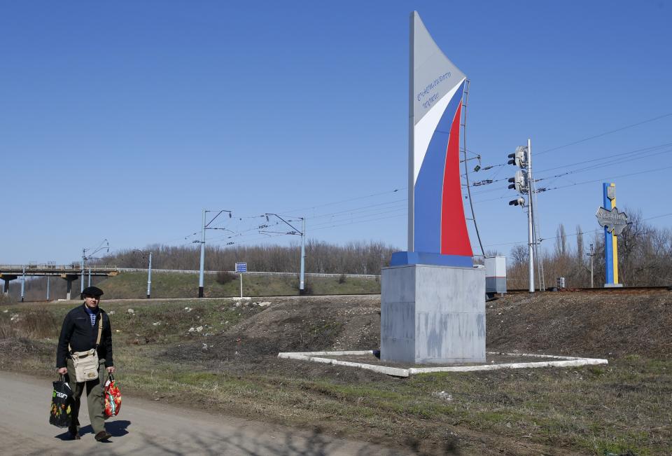 In this photo taken Monday, March 24, 2014, a man walks past a sign marking the border painted in colors of a Russian flag and reading "Have a good trip" in the village of Vyselki, eastern Ukraine. Ever since the 1991 breakup of the Soviet Union, the village of Vyselki has been split between Ukraine and Russia. For years its residents have continued to live together peacefully, doing most of their shopping in one country and paying their electricity bills in another. But after Russia seized the Crimean Peninsula from Ukraine, the Ukrainian villagers fear a further incursion of Russian troops, while the Russians say they would welcome their protection against the new pro-Western government in Kiev. (AP Photo/Sergei Grits)