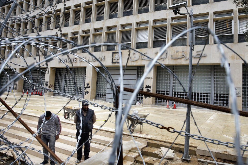 In this March 18, 2020 photo, workers stand outside the Lebanese Central Bank that has been shut down as part of the preventive measures against the coronavirus, in Beirut, Lebanon. Wealthier Western countries are considering how to ease lockdown restrictions and start taking gradual steps toward reviving business and daily life. But many developing countries, particularly in the Middle East and Africa, can hardly afford the luxury of any misstep. Consider tiny Lebanon, a country teetering on the abyss of bankruptcy with a fragile health system, a restless population and no tools for mapping a way out of the pandemic. (AP Photo/Bilal Hussein)
