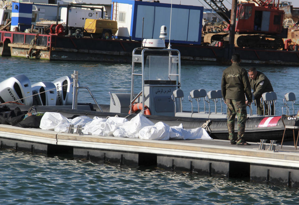 Tunisian coast guards stand next to the clovered dead bodies of migrants in the port of Sfax, central Tunisia, Thursday, Dec. 24, 2020. About 20 African migrants were found dead Thursday after their smuggling boat sank in the Mediterranean Sea while trying to reach Europe, Tunisian authorities said. Coast guard boats and local fishermen found and retrieved the bodies in the waters off the coastal city of Sfax in central Tunisia. (AP Photo/Houssem Zouari)