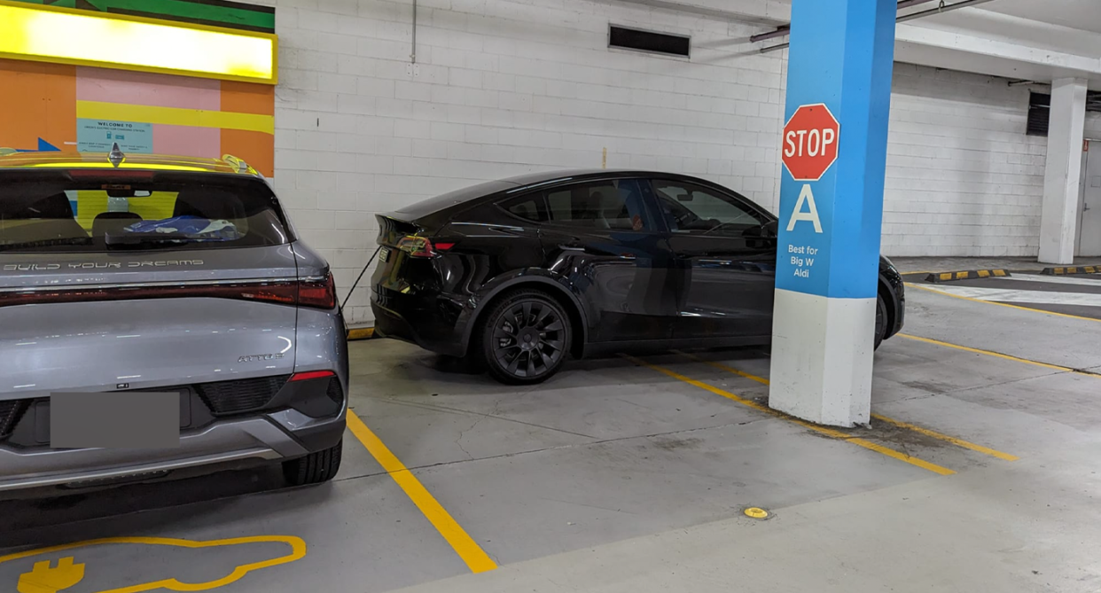 The black Tesla parked across two parking bays hooked into a charger beside another electric vehicle in the designated parking bay.