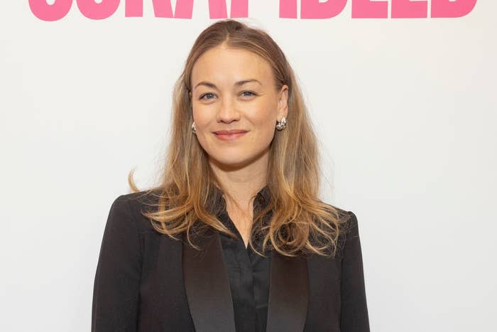 Yvonne in blazer smiling against a promotional backdrop