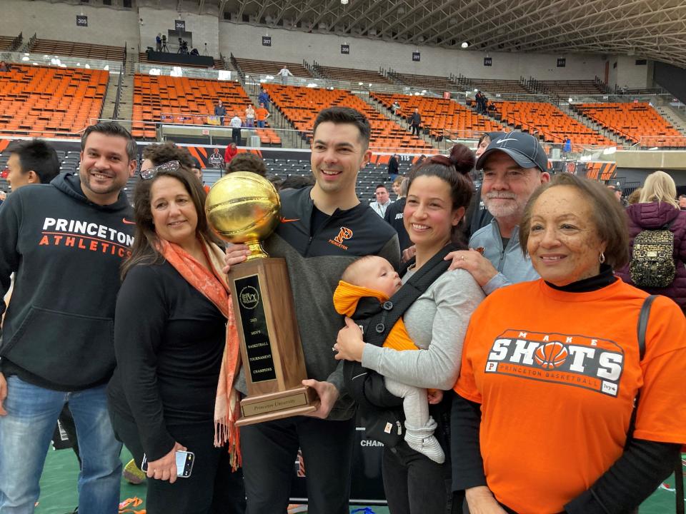 Princeton baseball associate head coach Brett MacConnell, surrounded by family members, holds the Ivy League Tournament trophy at Jadwin Gym. To his left are his wife Sarah and their 7-month-old son Cooper. His father Kevin MacConnell (one from the right) is Rutgers football's chief of staff