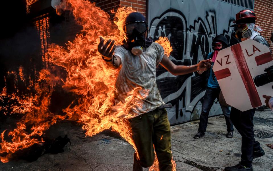 A demonstrator catches fire after the gas tank of a police motorbike exploded during clashes in a protest against Venezuelan President Nicolas Maduro - Credit: AFP